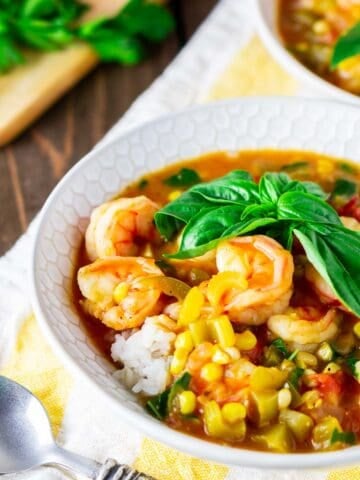 A bowl of summer shrimp étouffée with a spoon to the side on a yellow and white napkin.