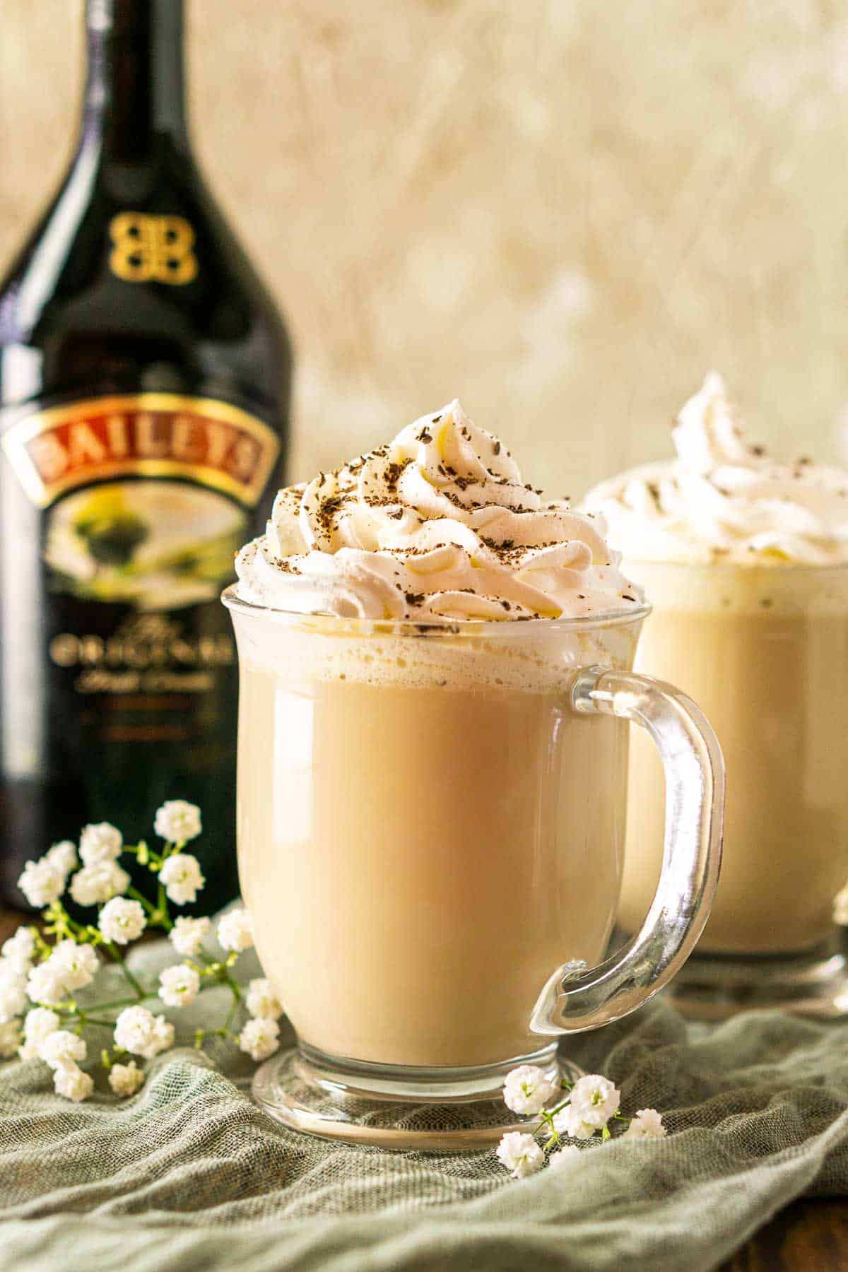 A Baileys latte on a green clothe with a bottle of Irish cream behind it.
