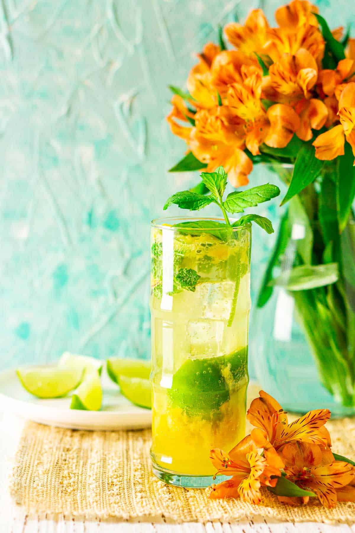 A mango mojito with an orange flower with a plate of limes in the background.