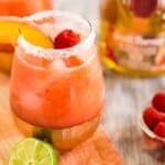 A raspberry-peach margarita on a colorful napkin with fruit around it.