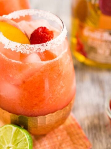 A raspberry-peach margarita on a colorful napkin with fruit around it.