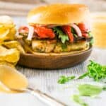 A salmon-avocado burger on a wooden plate with chips.