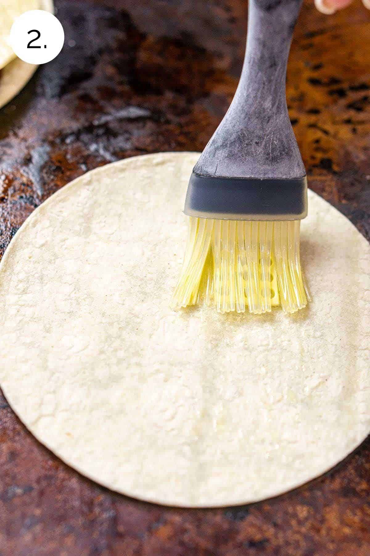 Using a pastry brush to coat the corn tortillas with a layer of olive oil.