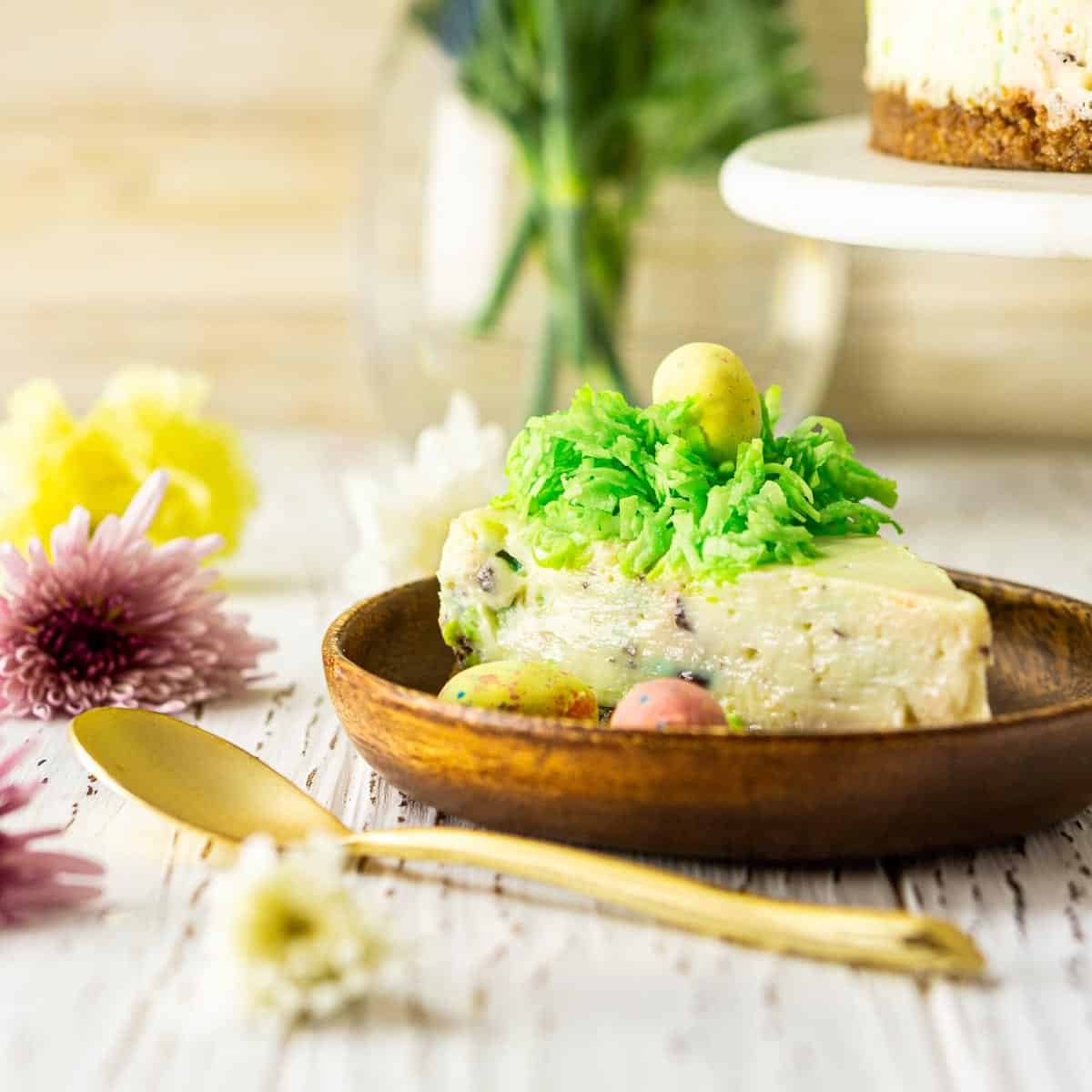 A slice of Easter cheesecake in a wooden plate with flowers to the side.