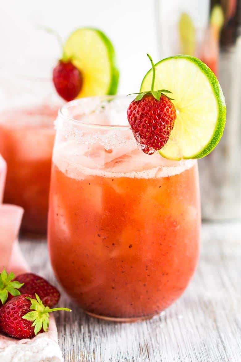 A roasted strawberry margarita on a white wooden board with a pink napkin to the left.