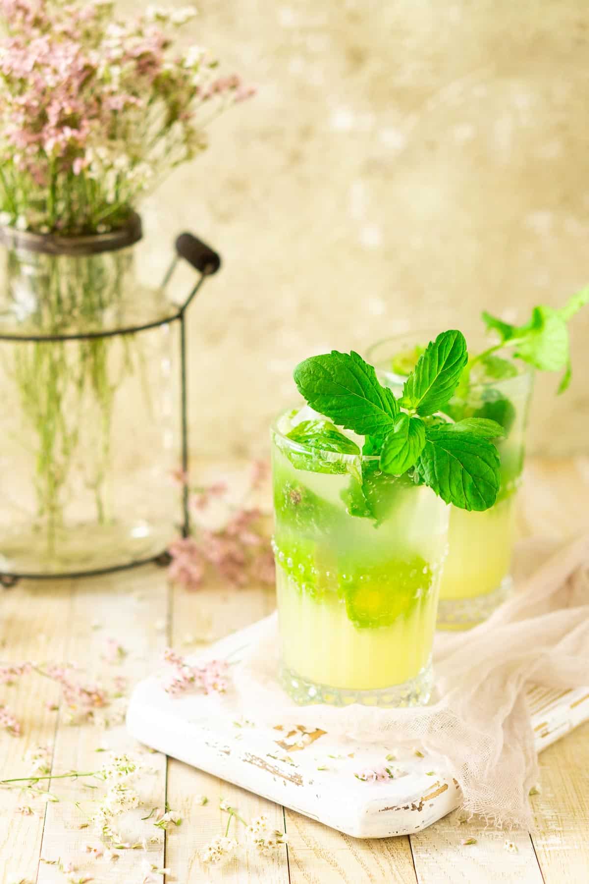 Two ginger mojitos on a white tray with flowers surrounding them.