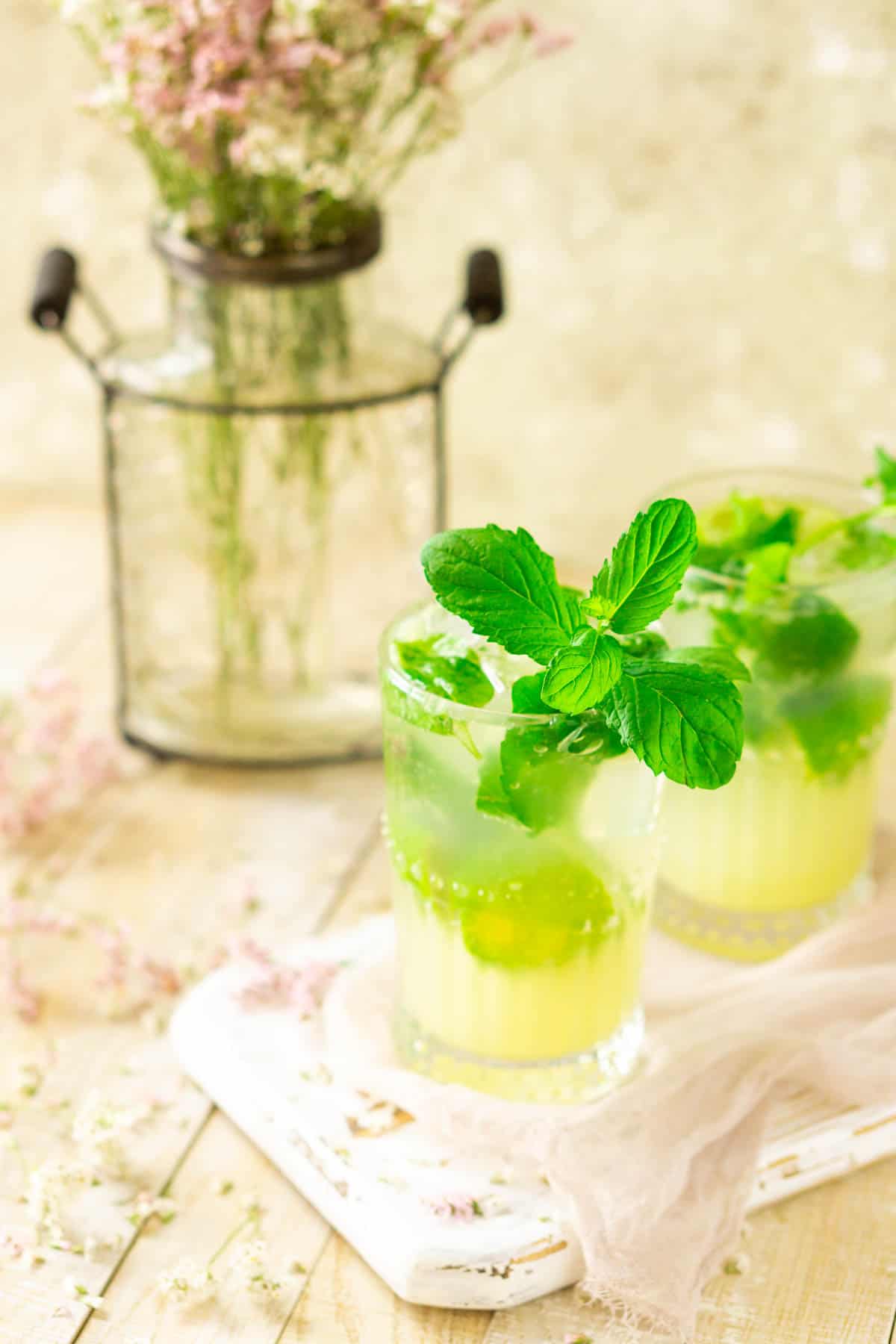 A side view of the ginger mojito on a white tray with flowers around it.