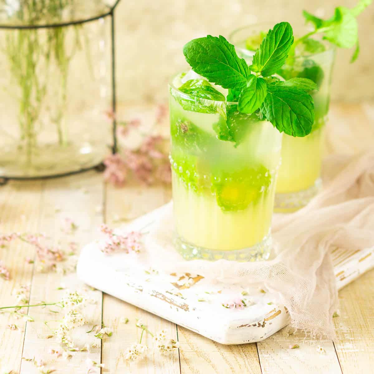 Two ginger mojitos on a white wooden board with flowers around them.