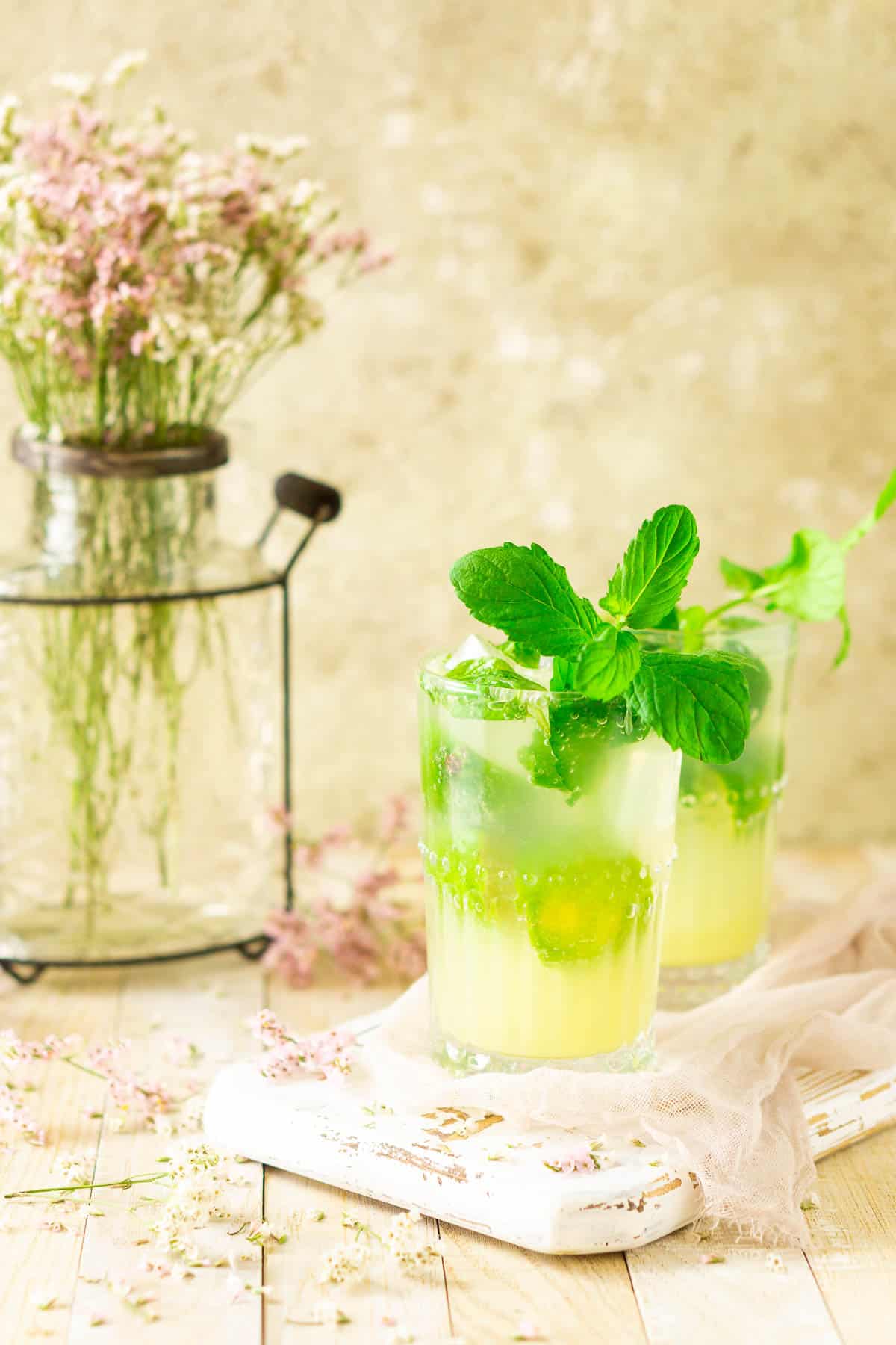 Looking straight on to two ginger mojitos with purple and white flowers behind them.