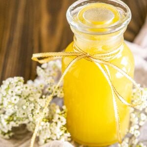 A glass of fresh ginger simple syrup with white flowers surrounding it on a piece of cheesecloth.