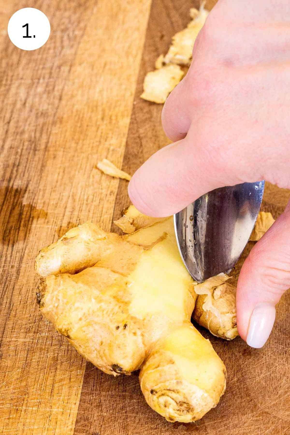 Peeling the ginger on a cutting board with a silver spoon.