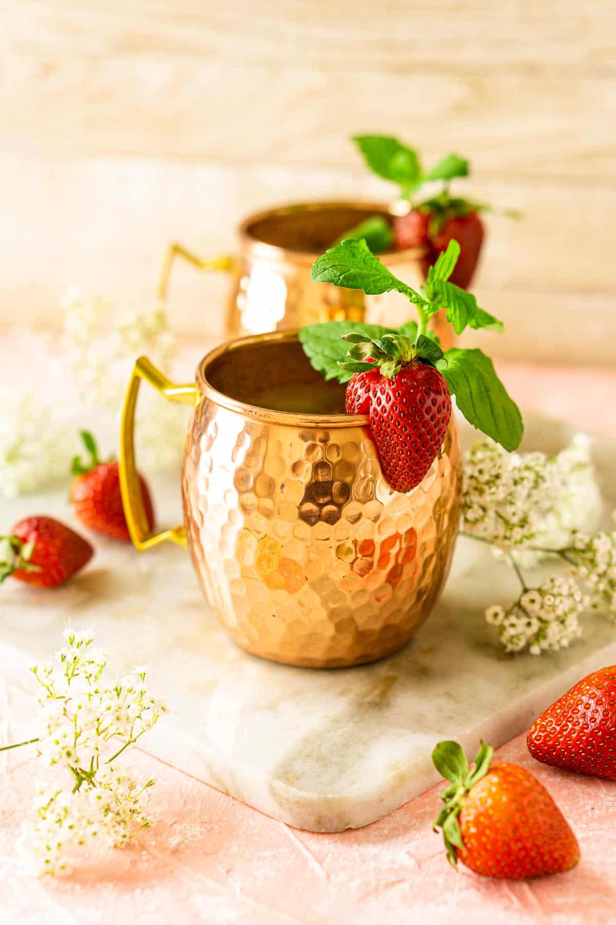 Two strawberry Moscow mules in copper mugs with fresh mint, lime slices and strawberries on the side.