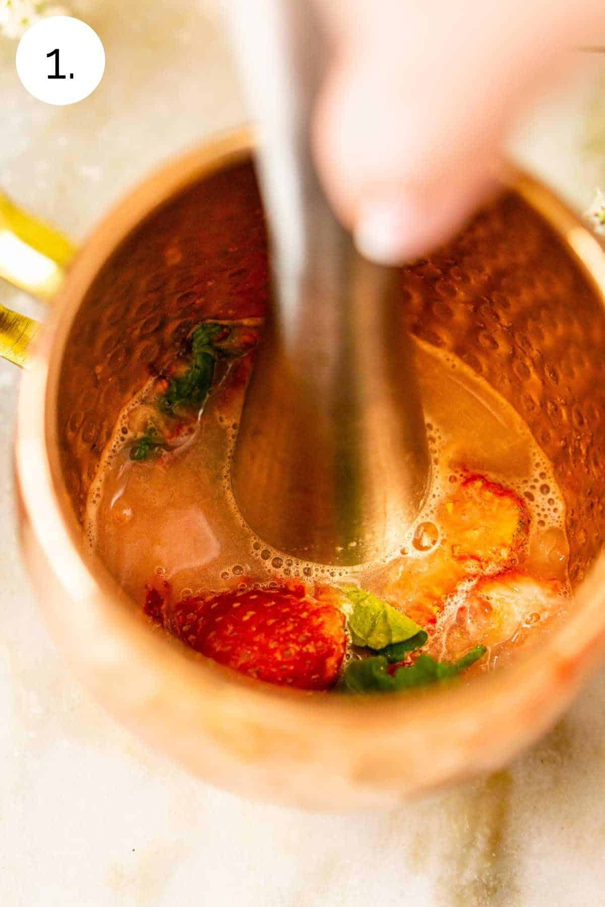 Muddling the mint with strawberries and lime juice in a copper mug.