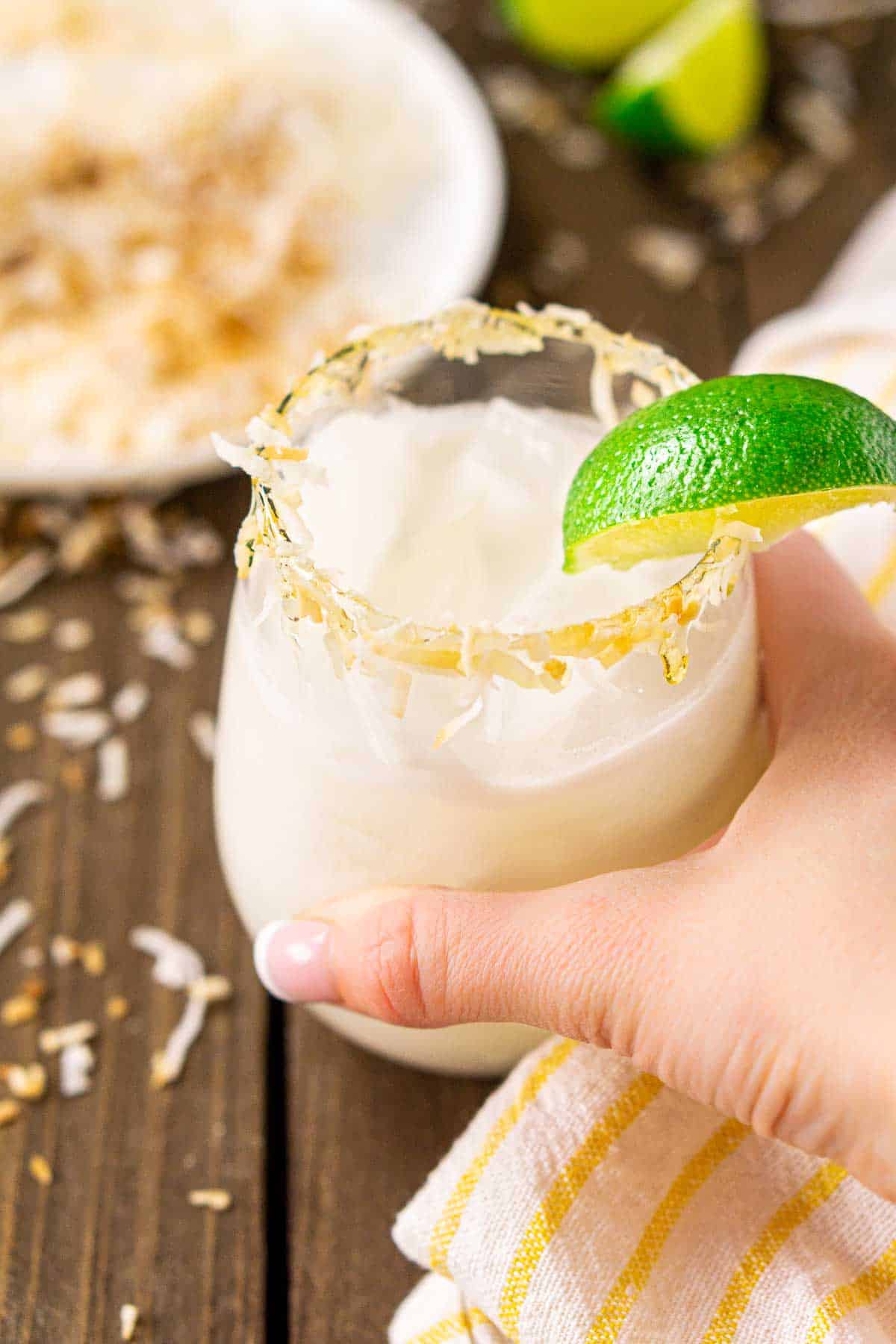 A hand grabbing a coconut margarita with toasted coconut around it.