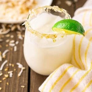 A coconut margarita on a wooden board with a white and yellow napkin to the side.