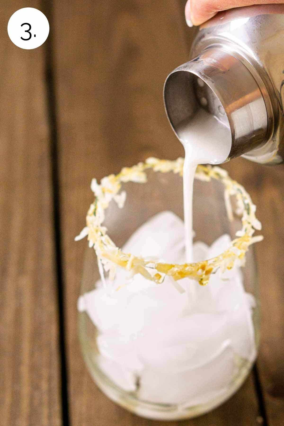 Straining the margarita into a glass with a coconut rim.