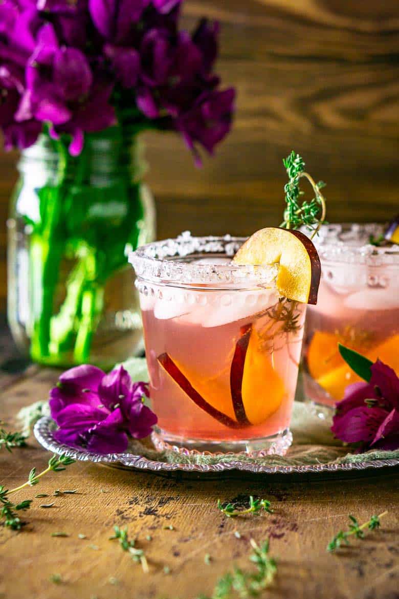 A plum margarita on a silver tray with fresh thyme and purple flowers around it.