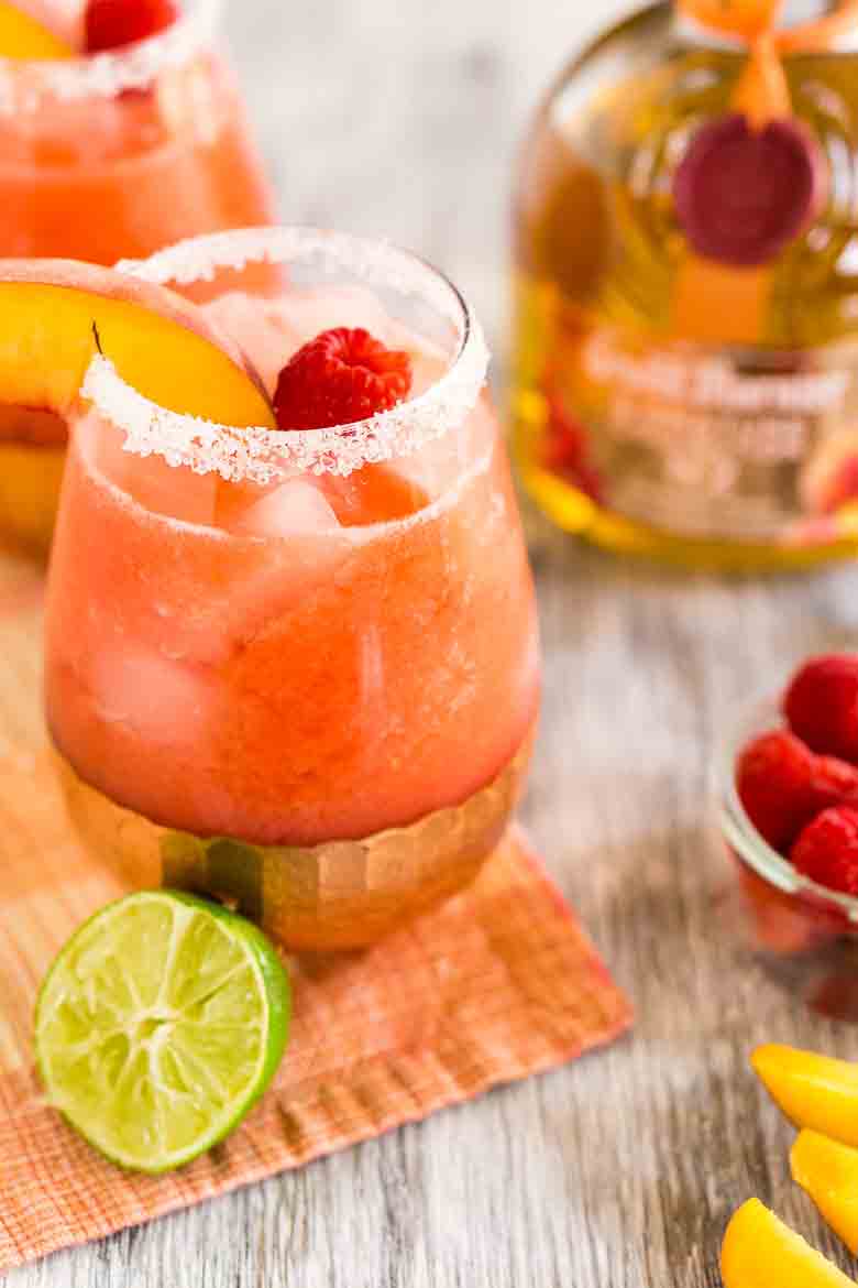 A fruity margarita with raspberry and peach purée on a colorful napkin with a lime in front.