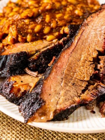 A close-up shot of the pellet grill brisket on a white plate with baked beans in the background.