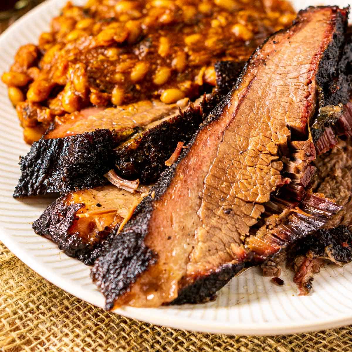 A close-up of the pellet grill brisket on a white plate with baked beans next to it.