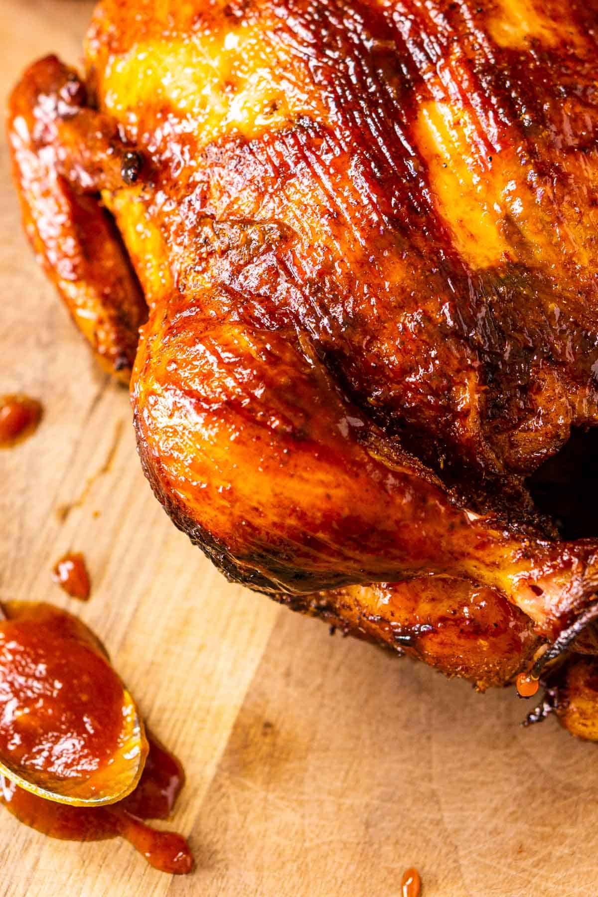 A close-up of the smoked whole chicken with BBQ sauce to the side.