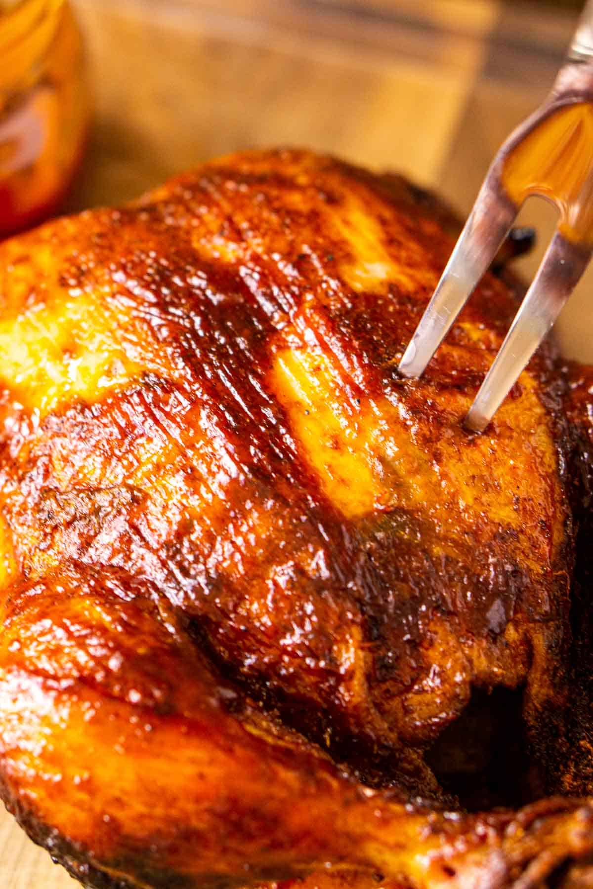 A carving fork stuck in the smoked chicken after resting and before cutting.