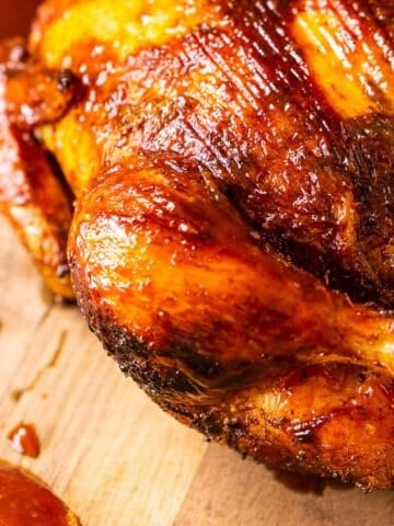 The smoked whole chicken on a cutting board with a spoon of BBQ sauce to the left.