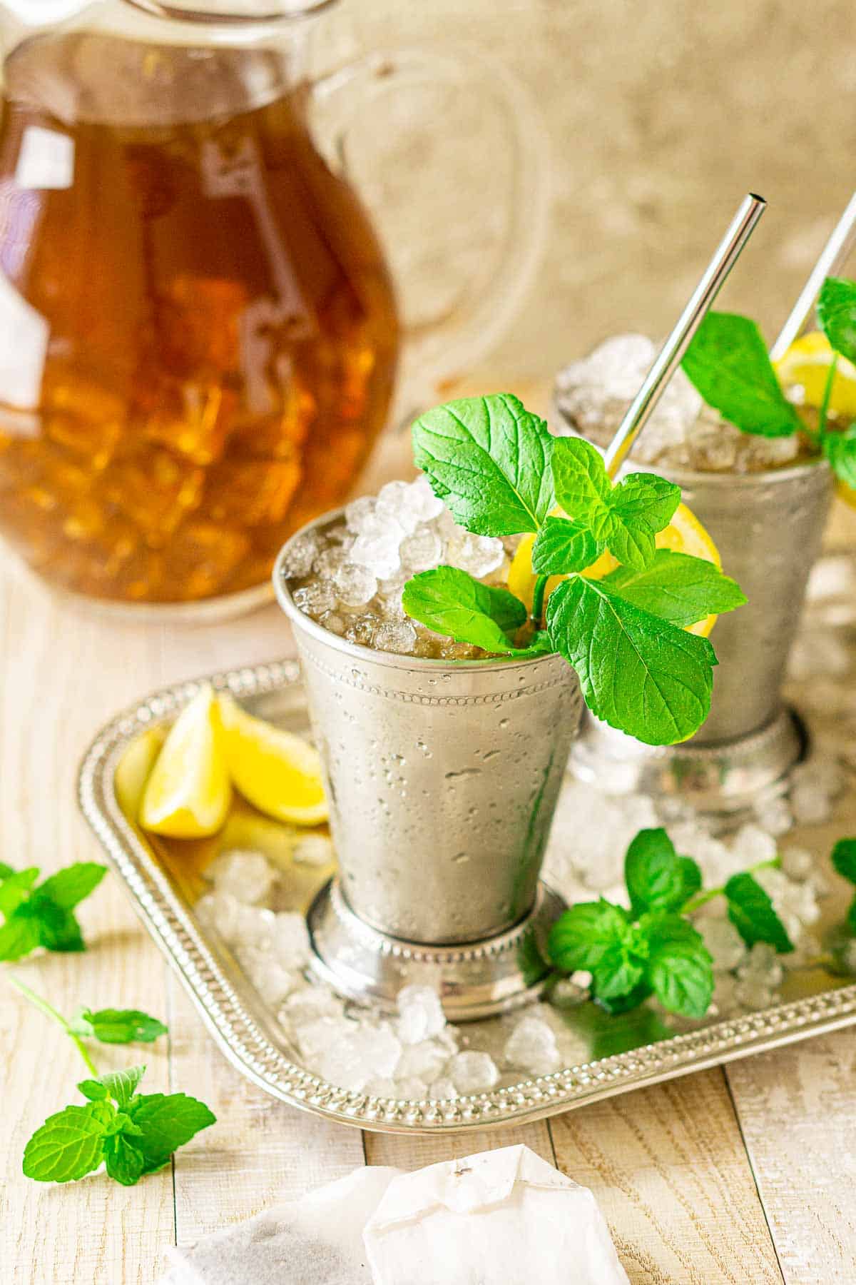 Looking down on two sweet tea mint juleps with crushed ice around them on a silver platter.