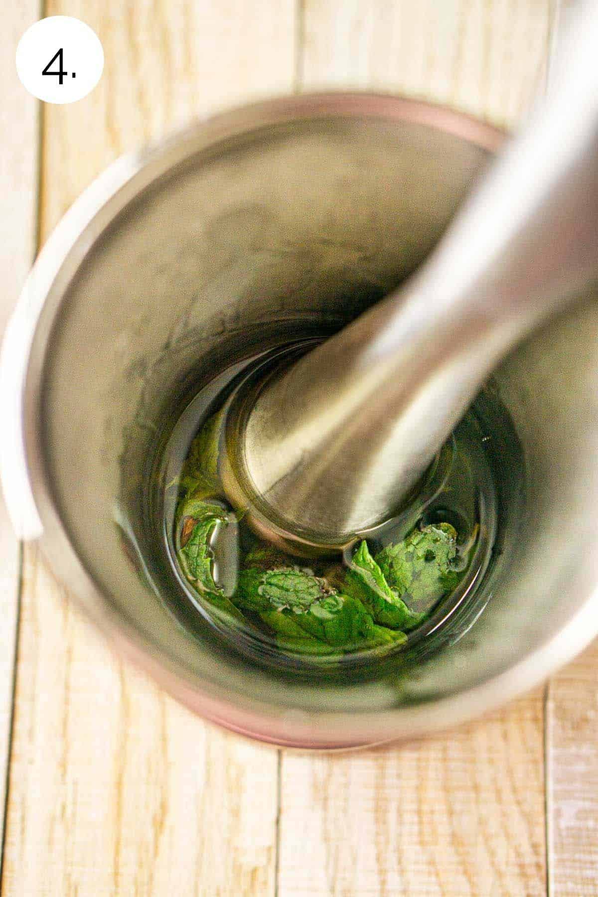 Muddling the bourbon and mint leaves in a silver pewter glass on a wooden surface.