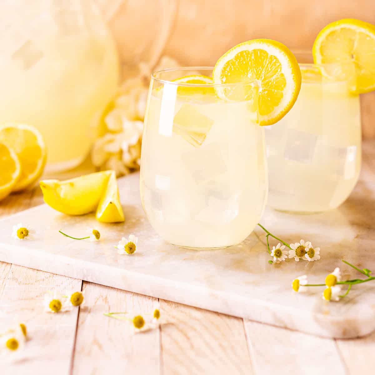 Two tequila lemonades on a white marble board with flowers around them.