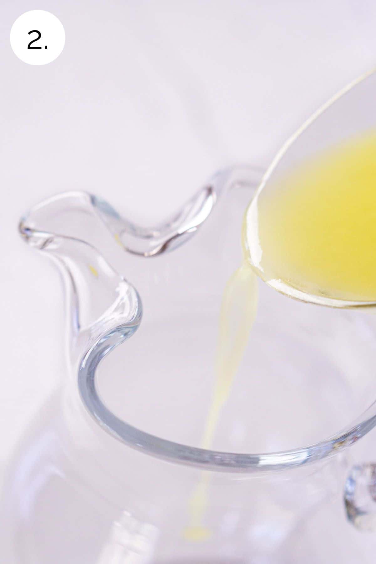 Pouring lemon juice into a clear pitcher on a white marble surface.
