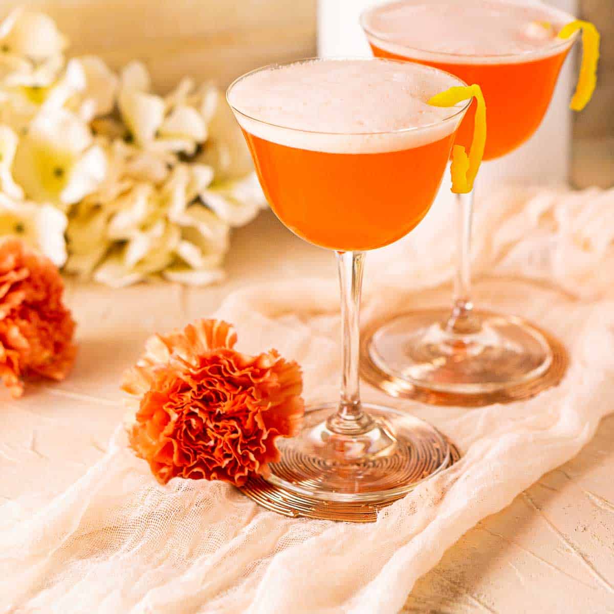 Two Aperol sour cocktails with orange flowers around them.