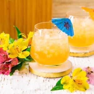 A Barbados rum punch on a white coaster with tropical flowers all around it.