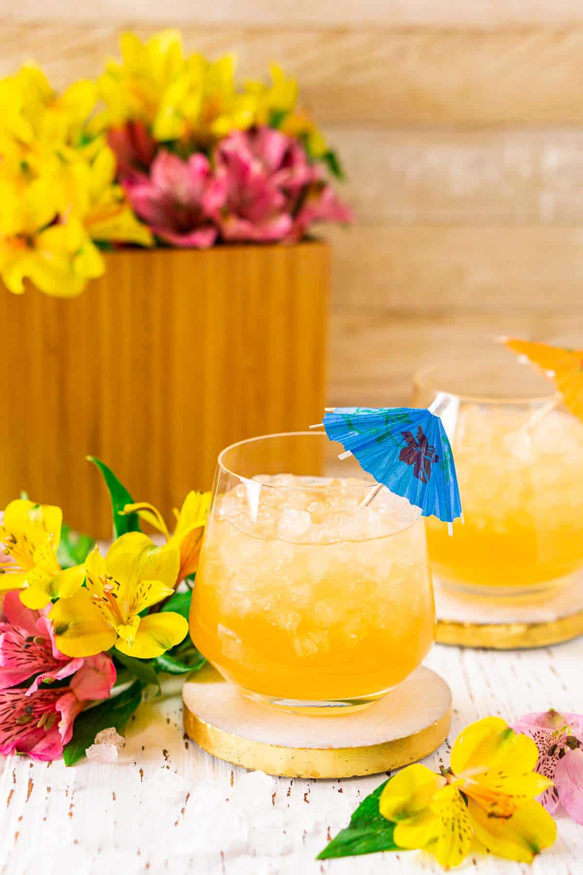 A Barbados rum punch on a white coaster with tropical flowers all around it.