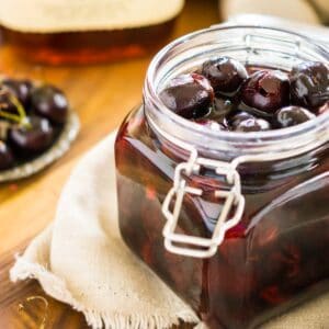 A jar of cherry-infused bourbon on a cream-colored clothe with cherries around it.