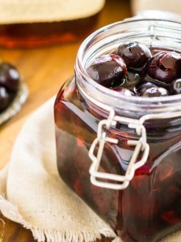 A jar of cherry-infused bourbon on a cream-colored clothe with cherries around it.