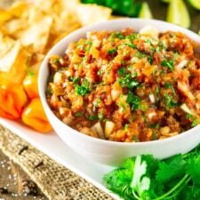 A bowl of jerk salsa on a white plate with cilantro around it.