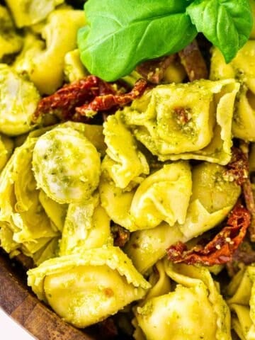 Looking down on a wooden bowl filled with the pesto tortellini salad.