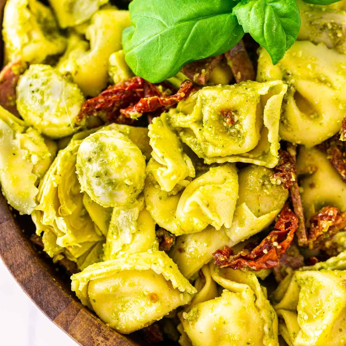 A bowl of pesto tortellini salad with a fresh basil sprig on top.