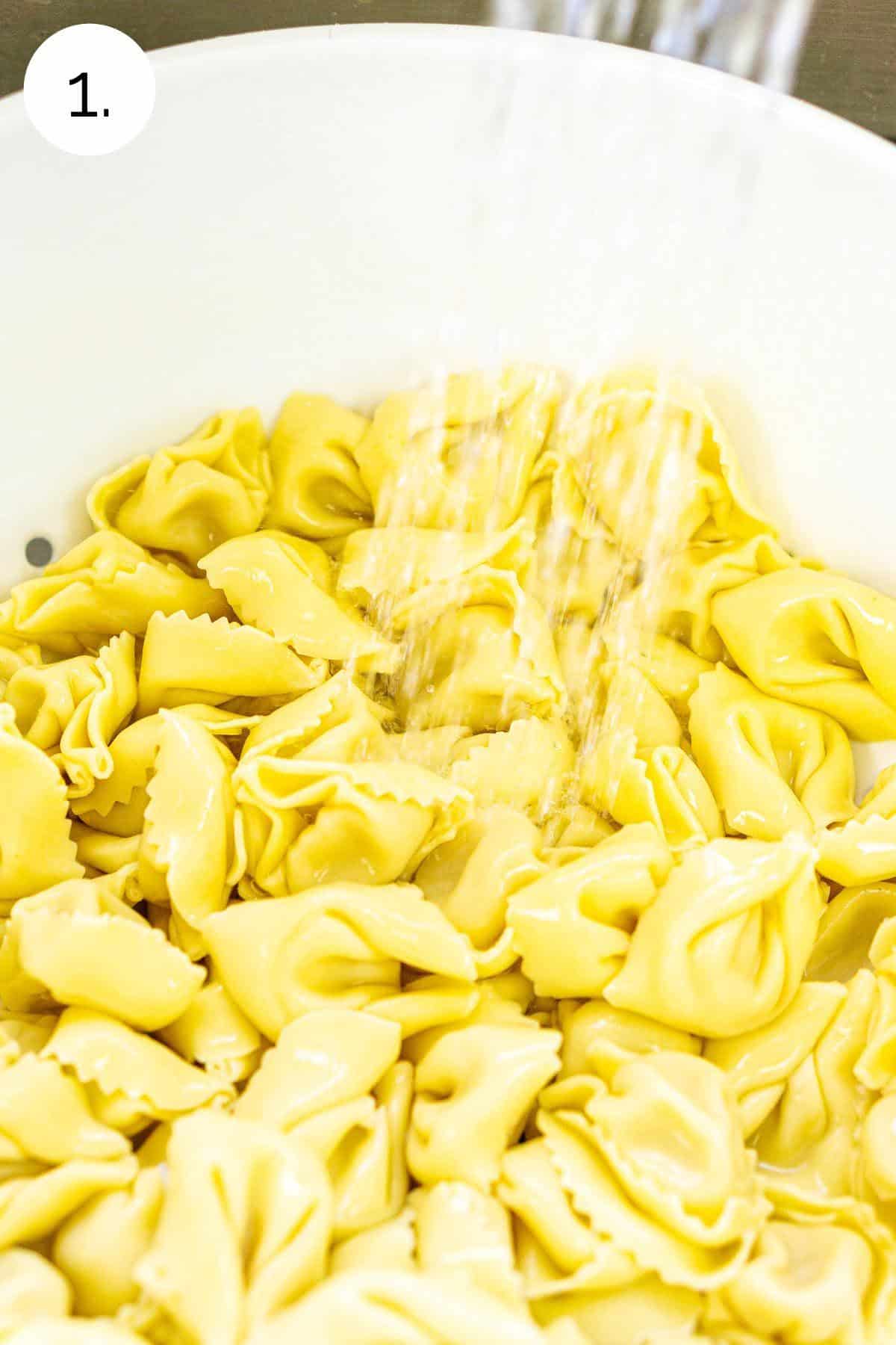Rinsing the fresh tortellini in a white strainer to chill and remove the extra starch.