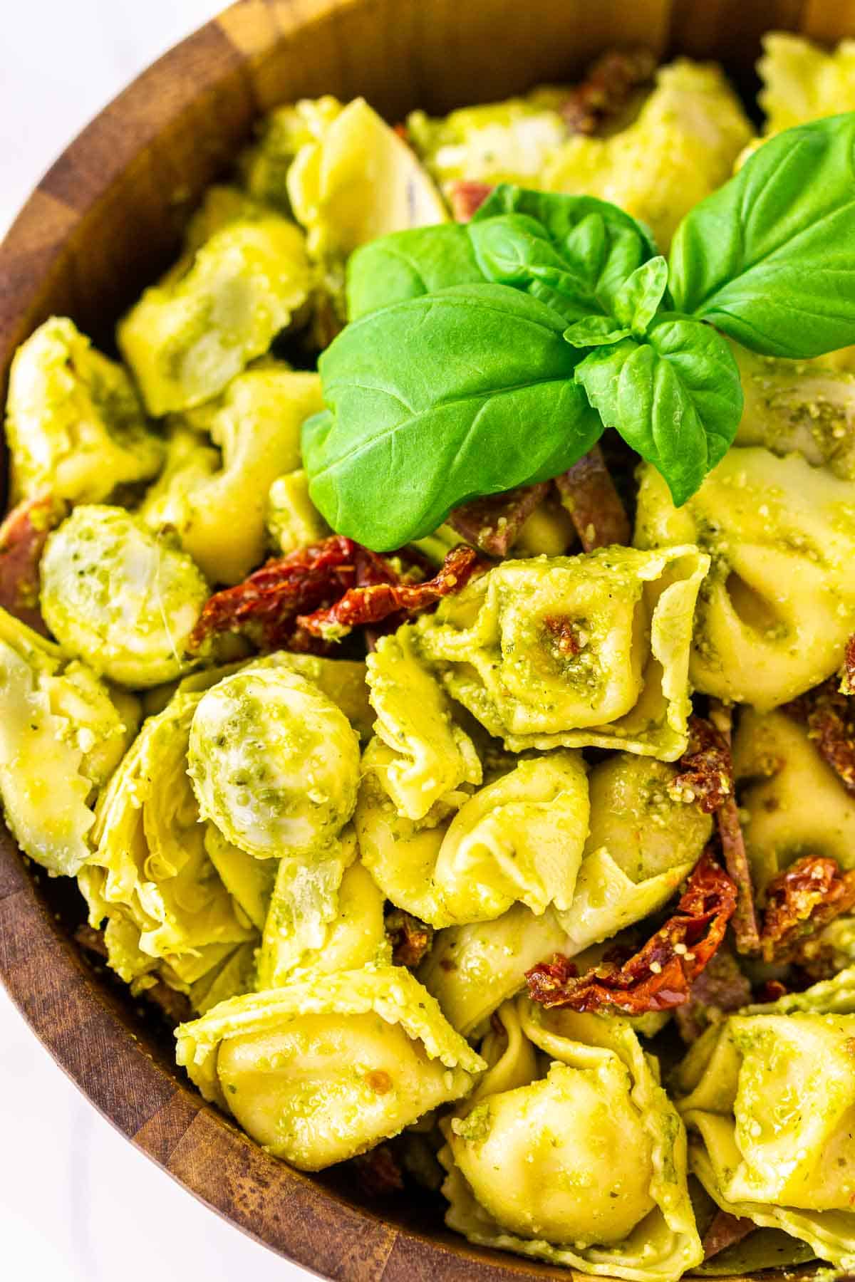 Looking down on a wooden bowl filled with the pesto tortellini salad.