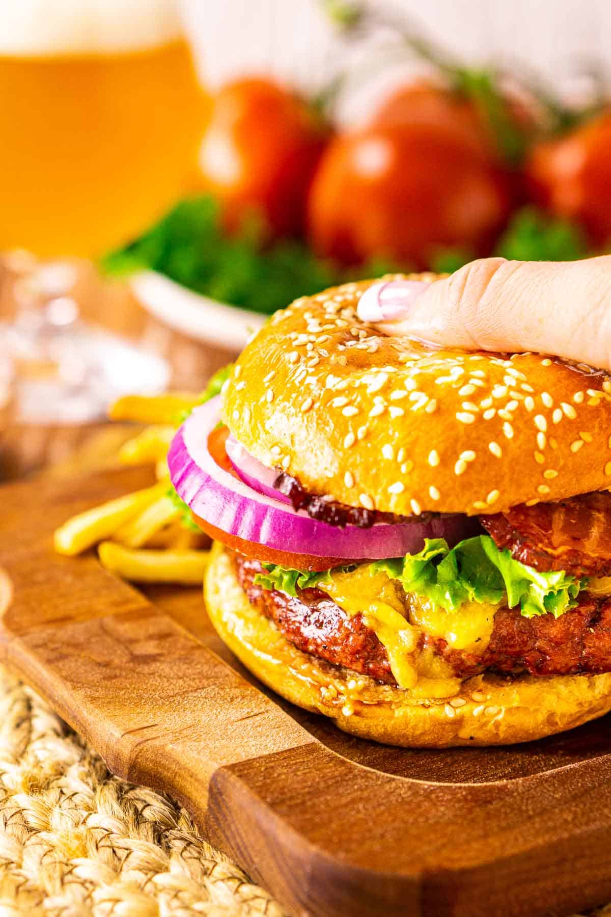 A hand grabbing the smoked burger off a wooden tray to take a bite.