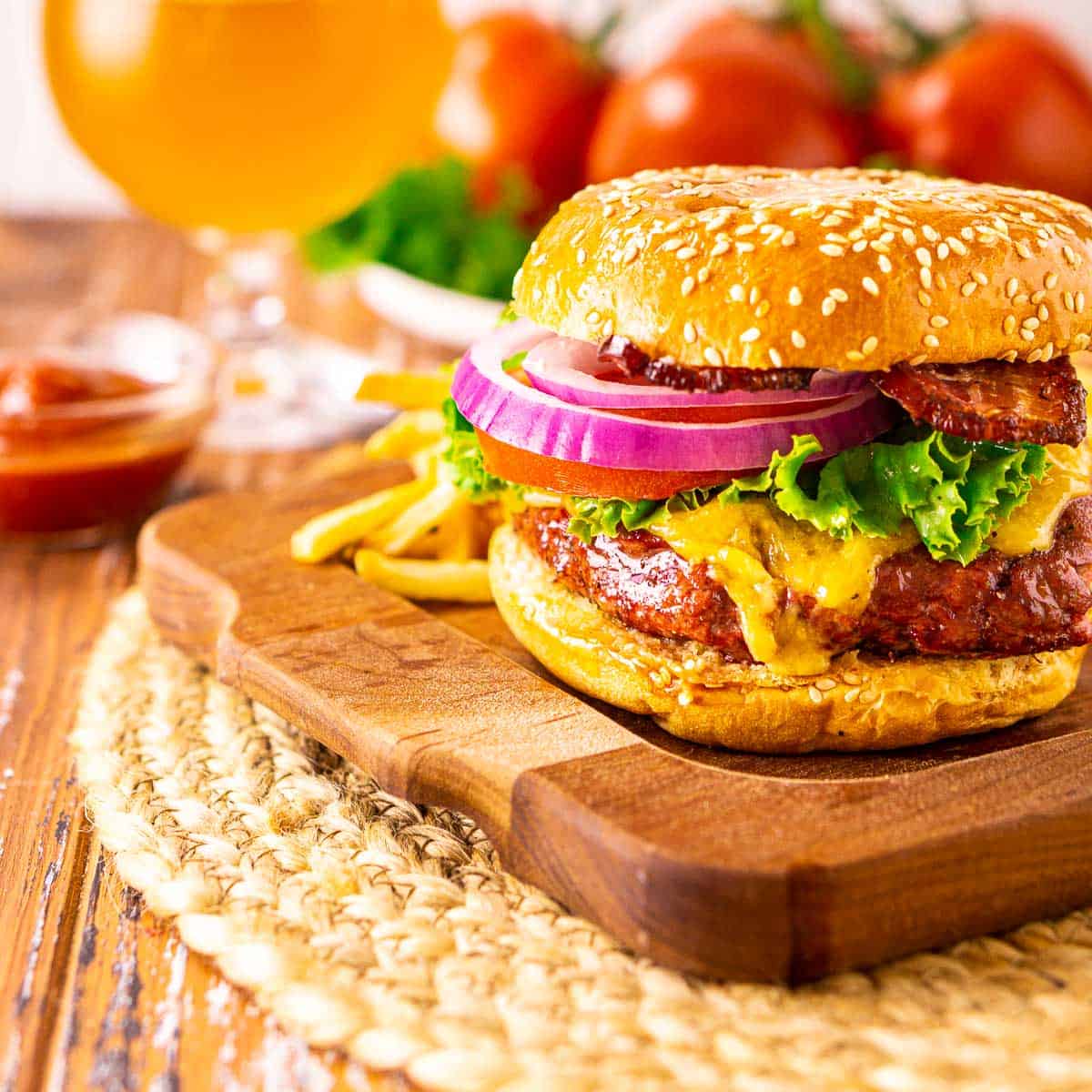 A smoked burger on a wooden tray with a beer in the background.