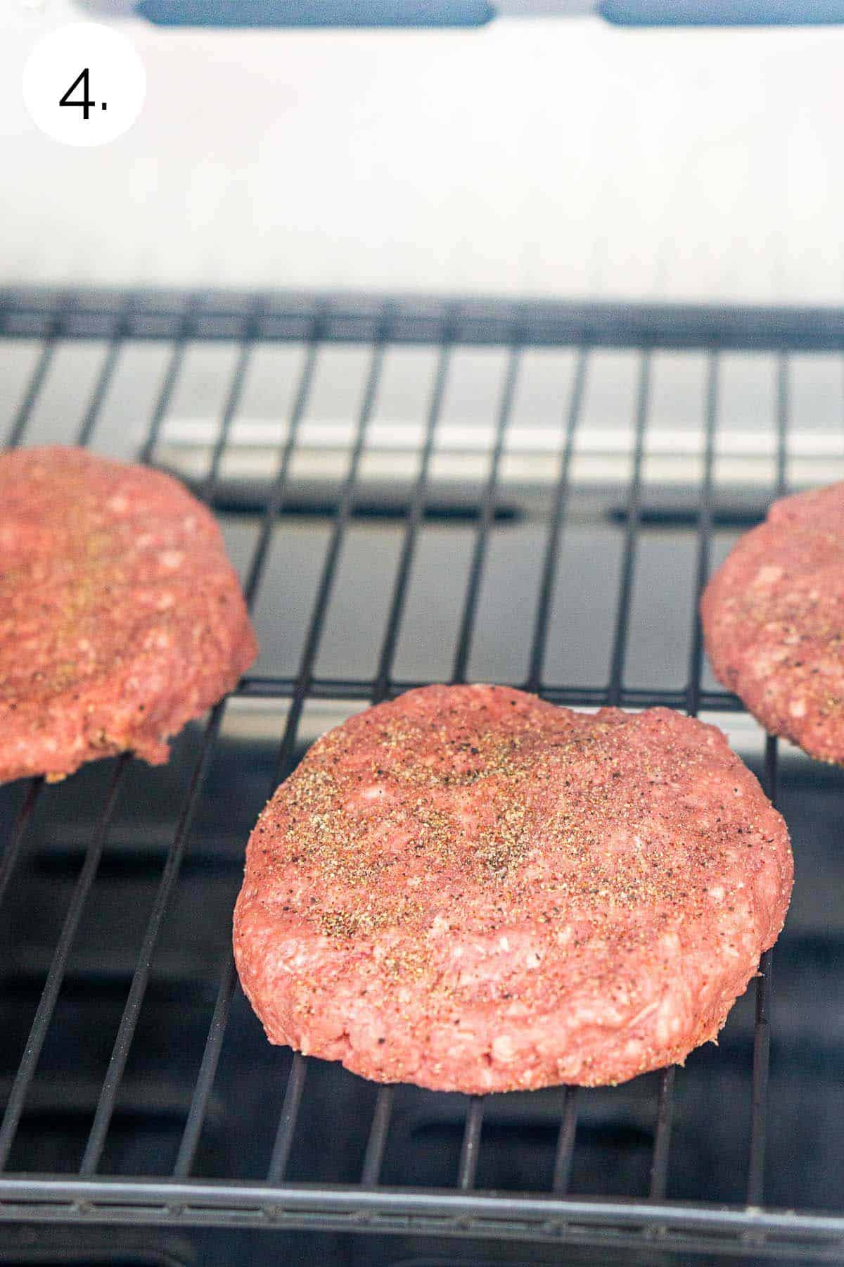 The burger patties on the grill grates before smoking.