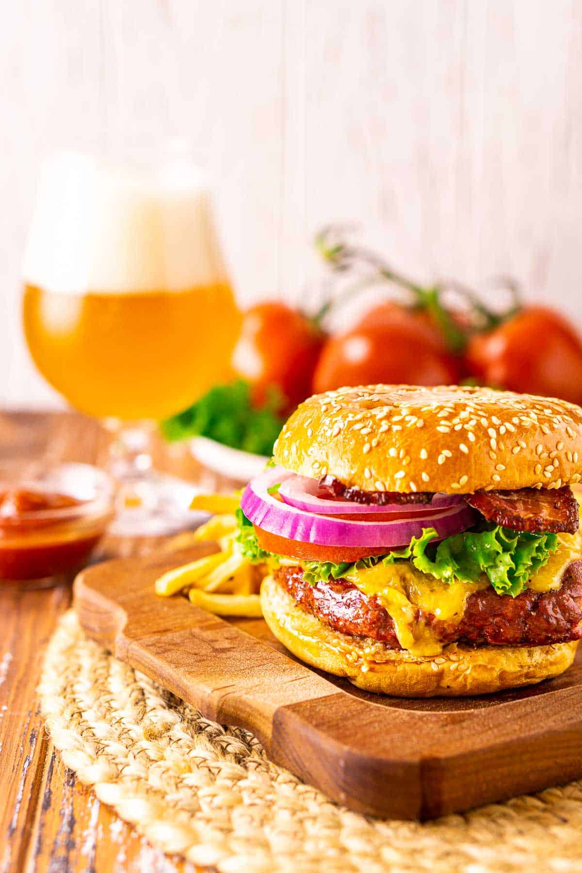 A smoked burger on a wooden surface with fries and a beer in the background.