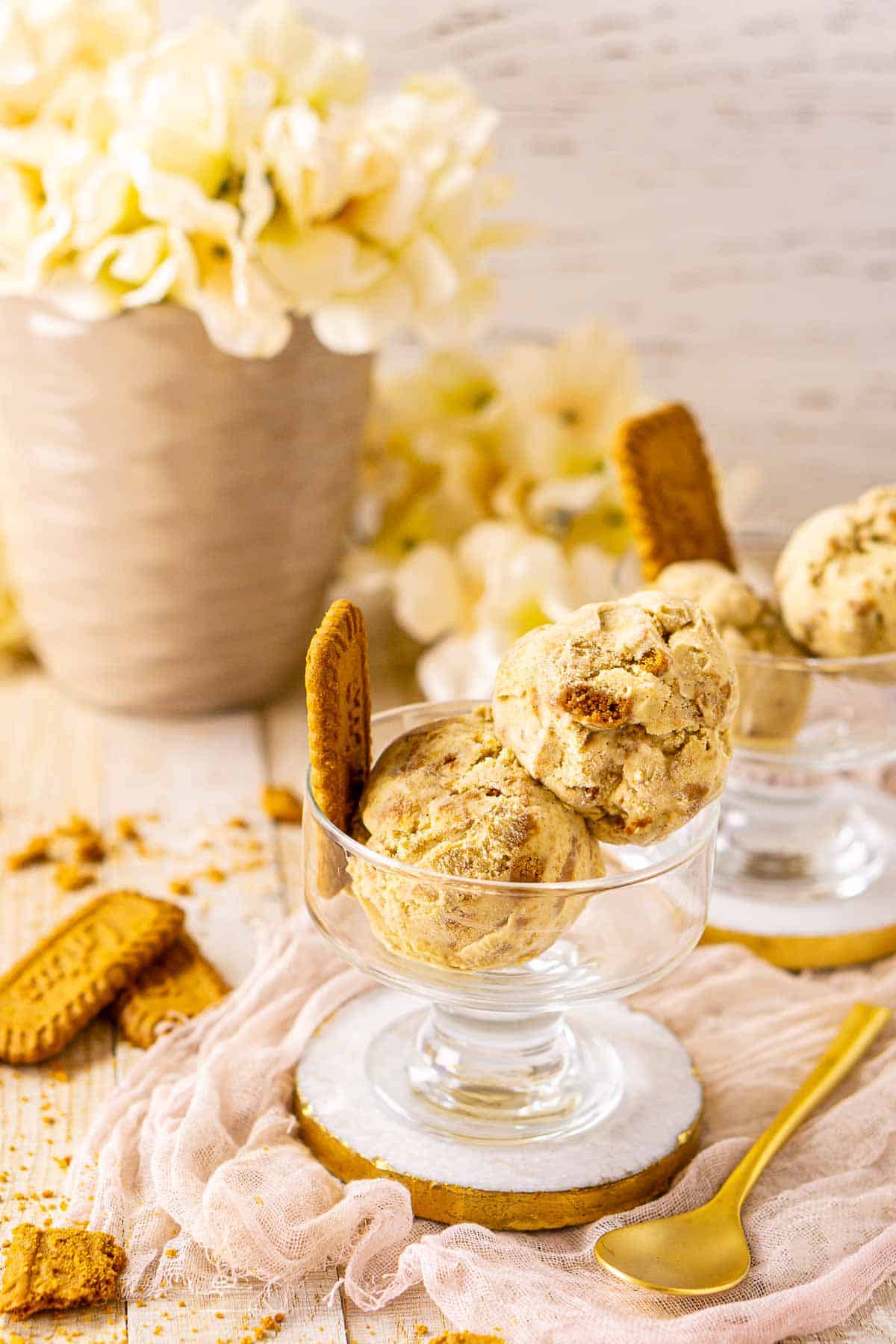 A side view of the Biscoff ice cream with a gold spoon to the right and white flowers in the background.