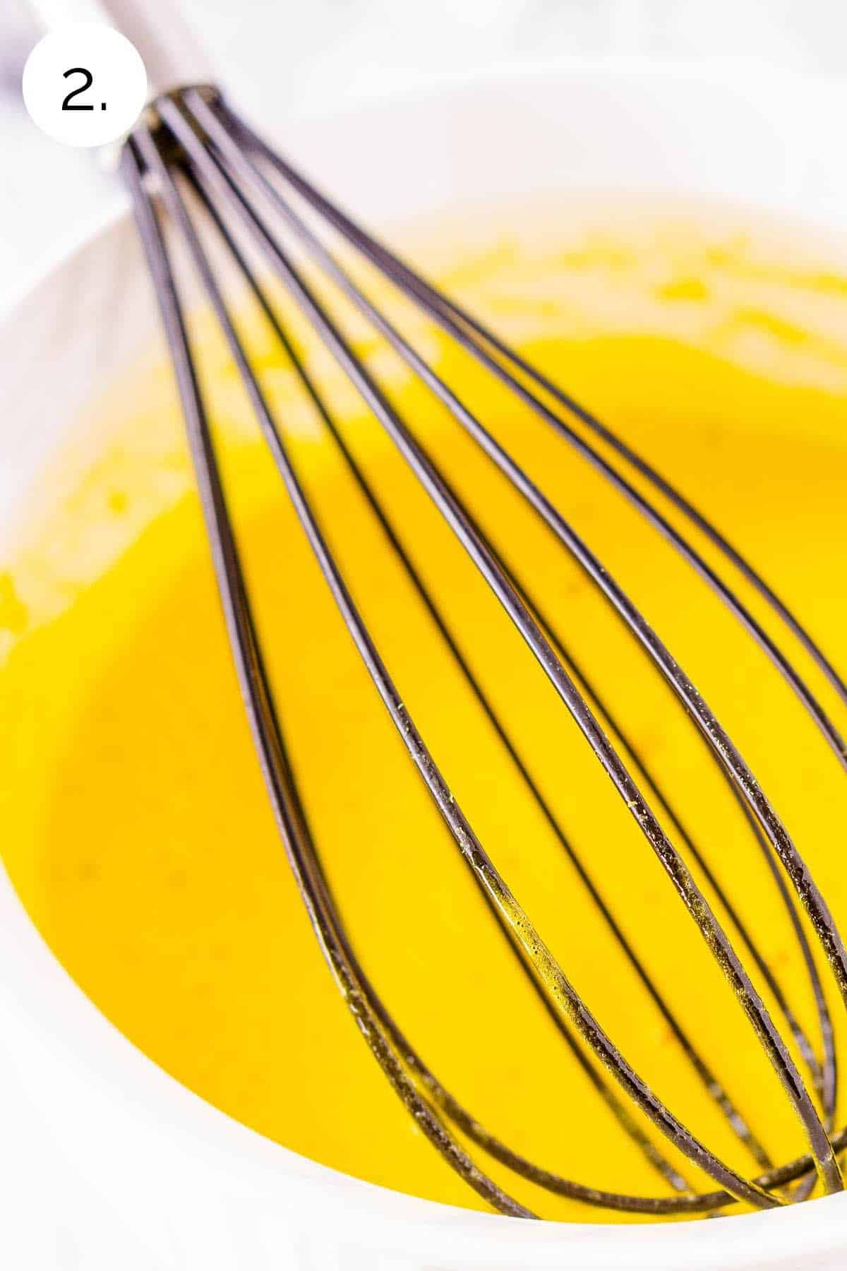 Whisking the egg yolks in a small white bowl against a white countertop.
