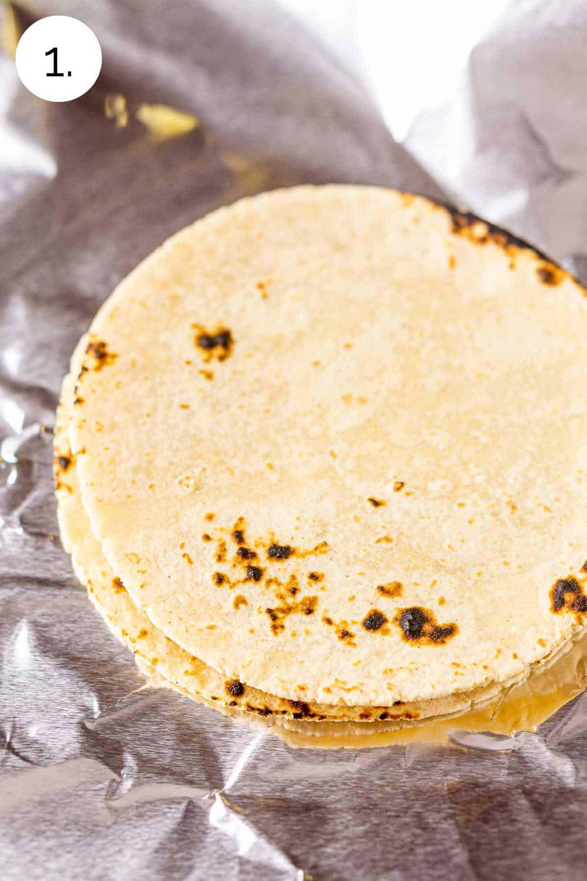 A stack of tortillas on aluminum foil before wrapping and warming in the oven.