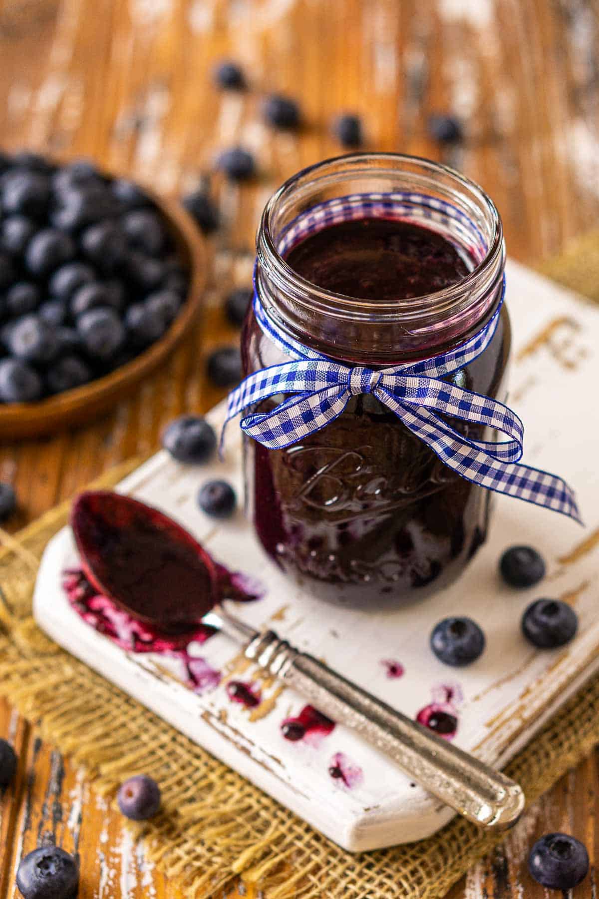 A jar of blueberry BBQ sauce on a white board with a spoon full of sauce in front of it.