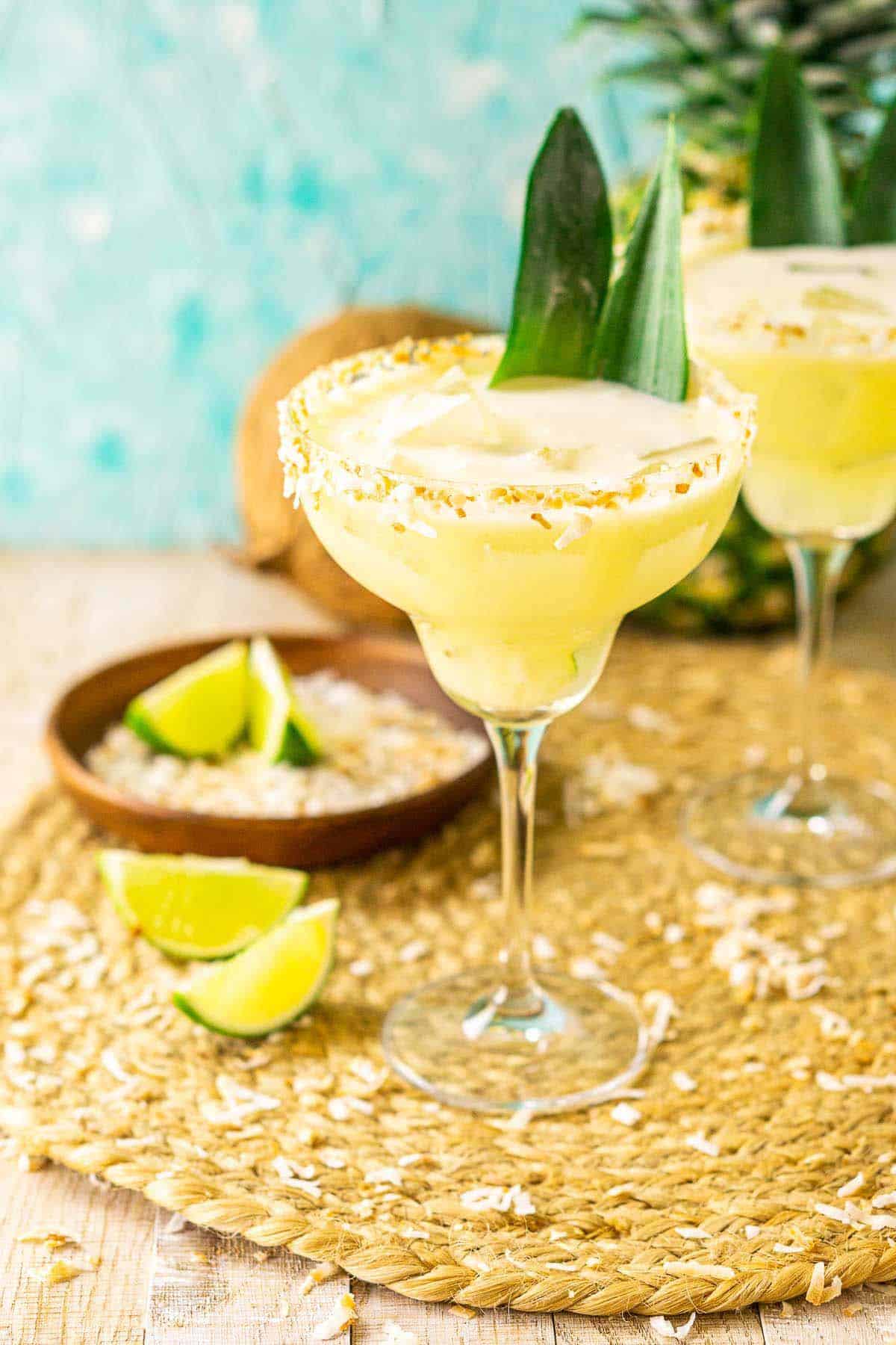 A pineapple-coconut margarita on a placemat with toasted coconut around it against a blue background.